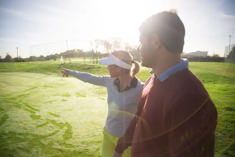 A man and woman communicating on a golf course, discussing strategy and enjoying the sunny day outdoors