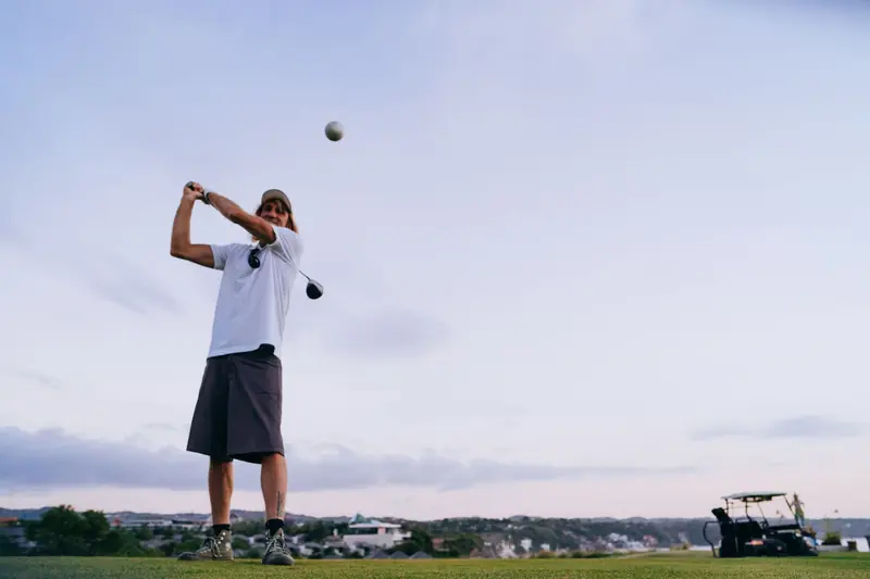A man swinging a golf club on a scenic outdoor course during the evening