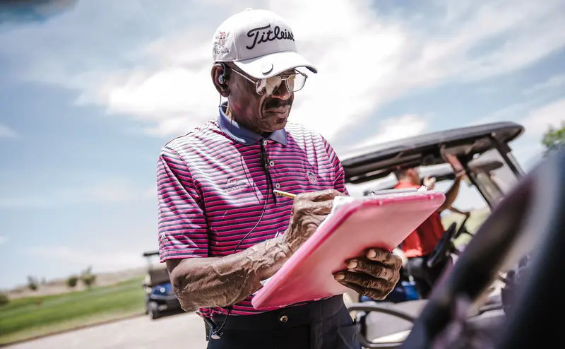 Senior man in golf attire writing on clipboard outdoors on a sunny day