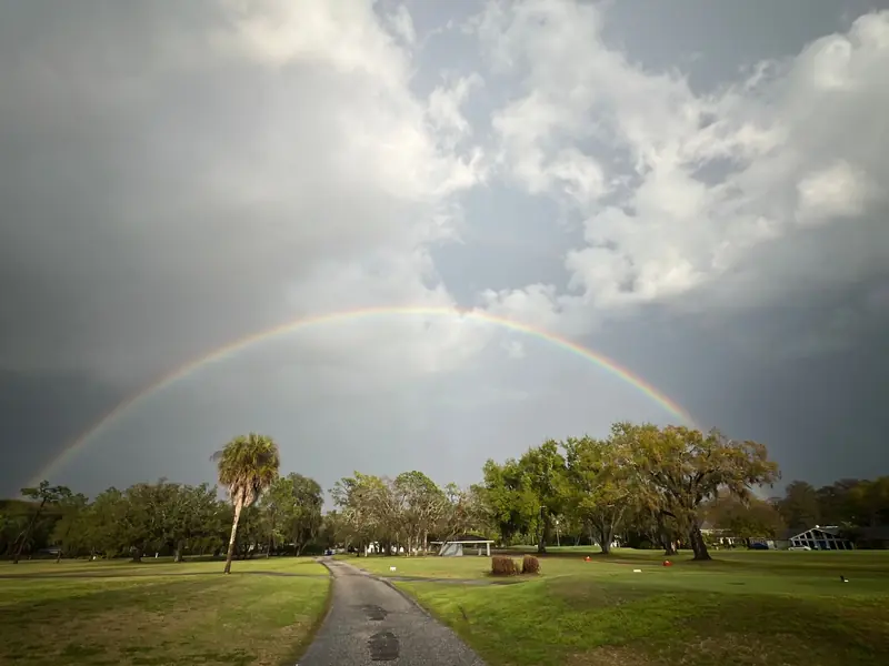 A brilliant rainbow arches over a tranquil golf course, creating a picturesque scene in a tropical landscape