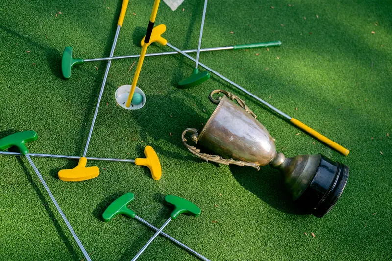 Colorful mini golf putters with a trophy on vibrant green turf, symbolizing victory