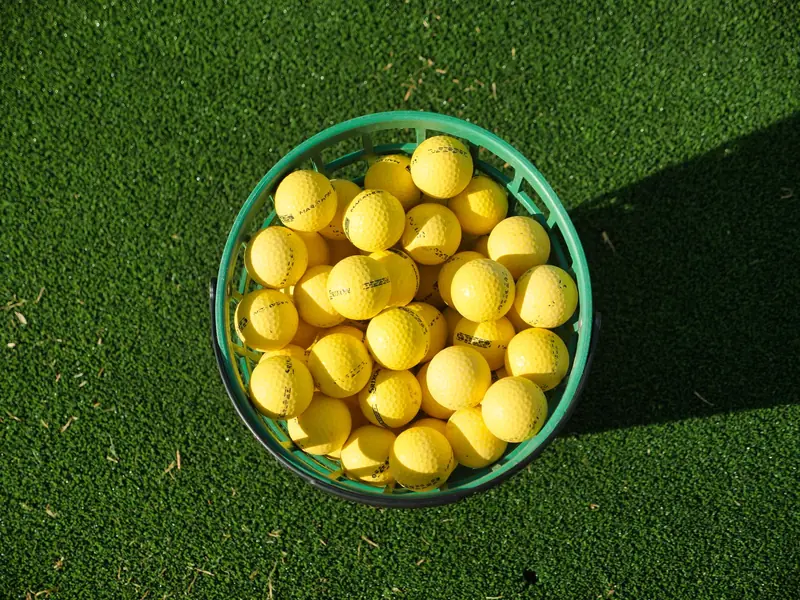 Top view of a basket filled with yellow golf balls placed on bright green artificial turf