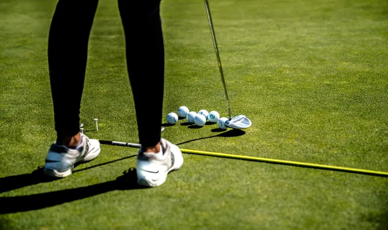 A golfer practicing putting on a sunny day with several golf balls on the green