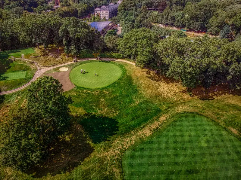 Aerial view of a lush golf course surrounded by trees, showcasing the vibrant greens under a sunny sky