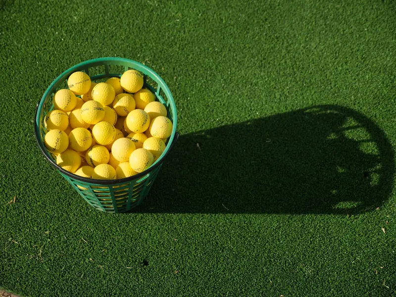 A basket full of yellow golf balls casting a shadow on vibrant green turf