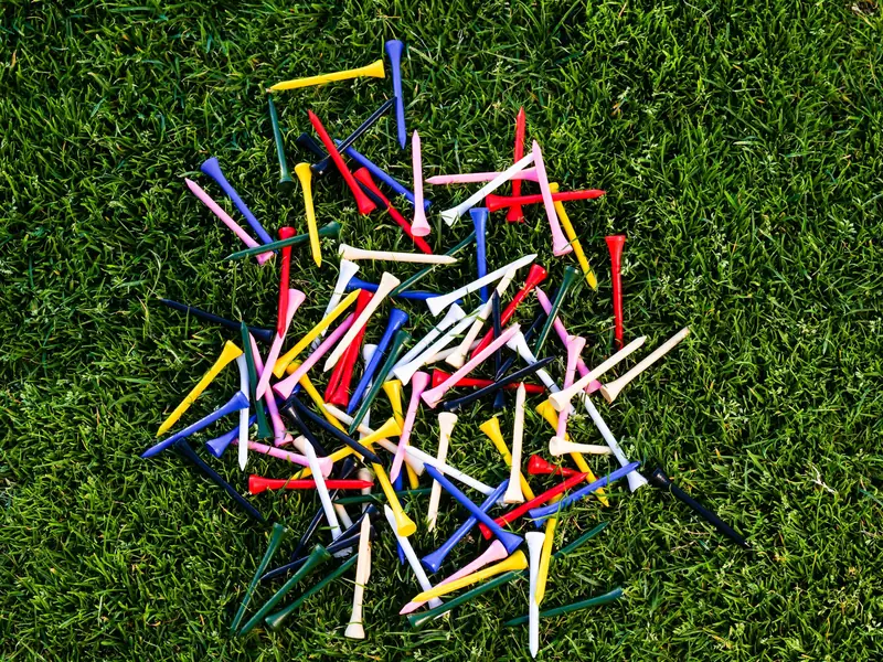 A colorful assortment of golf tees scattered on lush green grass, perfect for sports themes
