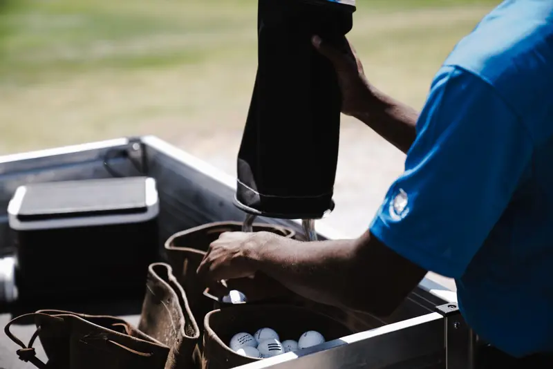 A man in a blue shirt organizing golf balls and leather bags outdoors on a sunny day