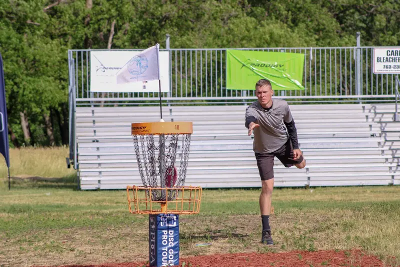A man throws a disc towards the basket during a disc golf tournament in Clearwater, MN