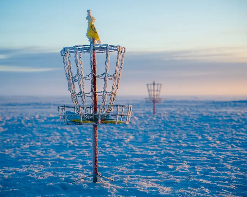 Frosty disc golf basket in a snowy open field during a winter sunrise, capturing serene outdoor vibes