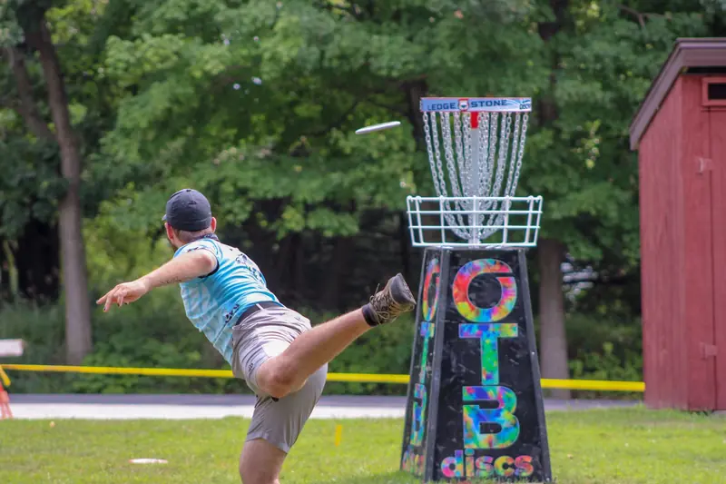 Man playing disc golf outdoors, expertly throwing frisbee towards basket in a lively game