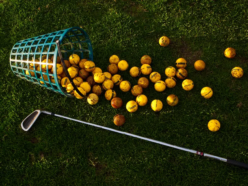 A basket of yellow golf balls spilled on green grass with a golf club nearby