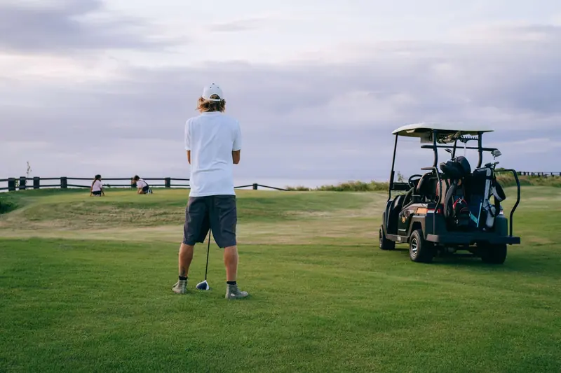 A golfer stands ready to play on a beautiful course with golf cart and clubs nearby