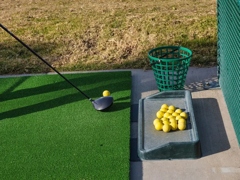 Golf driving range mat with club and yellow balls ready for practice