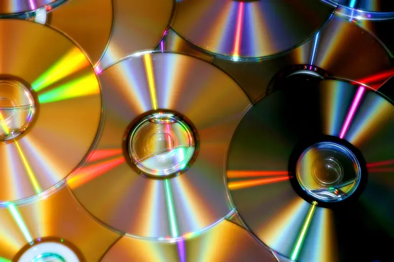 A close-up photo of compact discs reflecting colorful light patterns