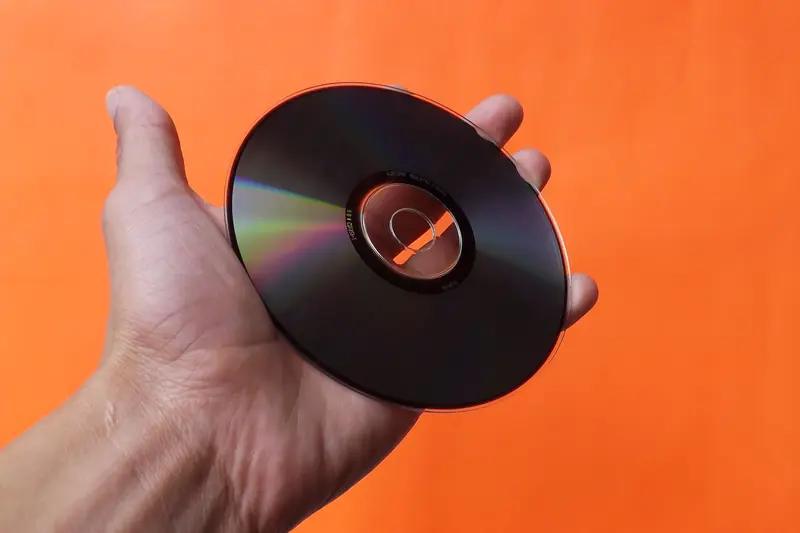 Close-up of a hand holding a classic compact disc with an orange background, evoking nostalgia