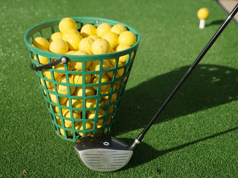 A close-up of a basket full of yellow golf balls with a golf club on green turf, ideal for sports imagery