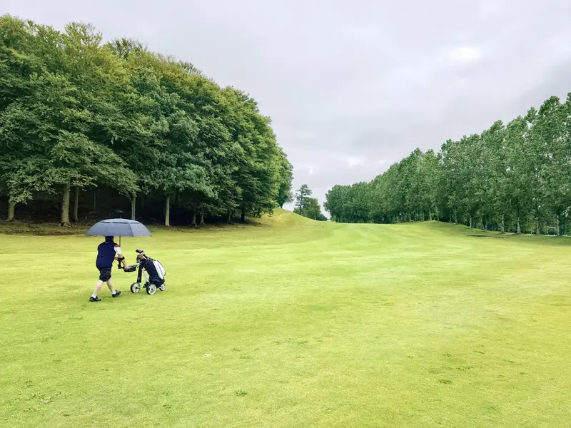 Man with umbrella and golf cart on a lush green golf course in Tuve, Sweden
